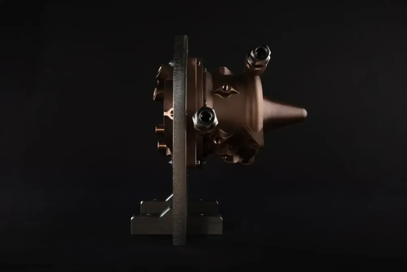 Ein metallisches, kegelförmiges mechanisches Bauteil mit mehreren Bolzen und hervorstehenden Verbindungsstücken, das auf einem dunklen Hintergrund dargestellt und von einem Metallständer getragen wird.