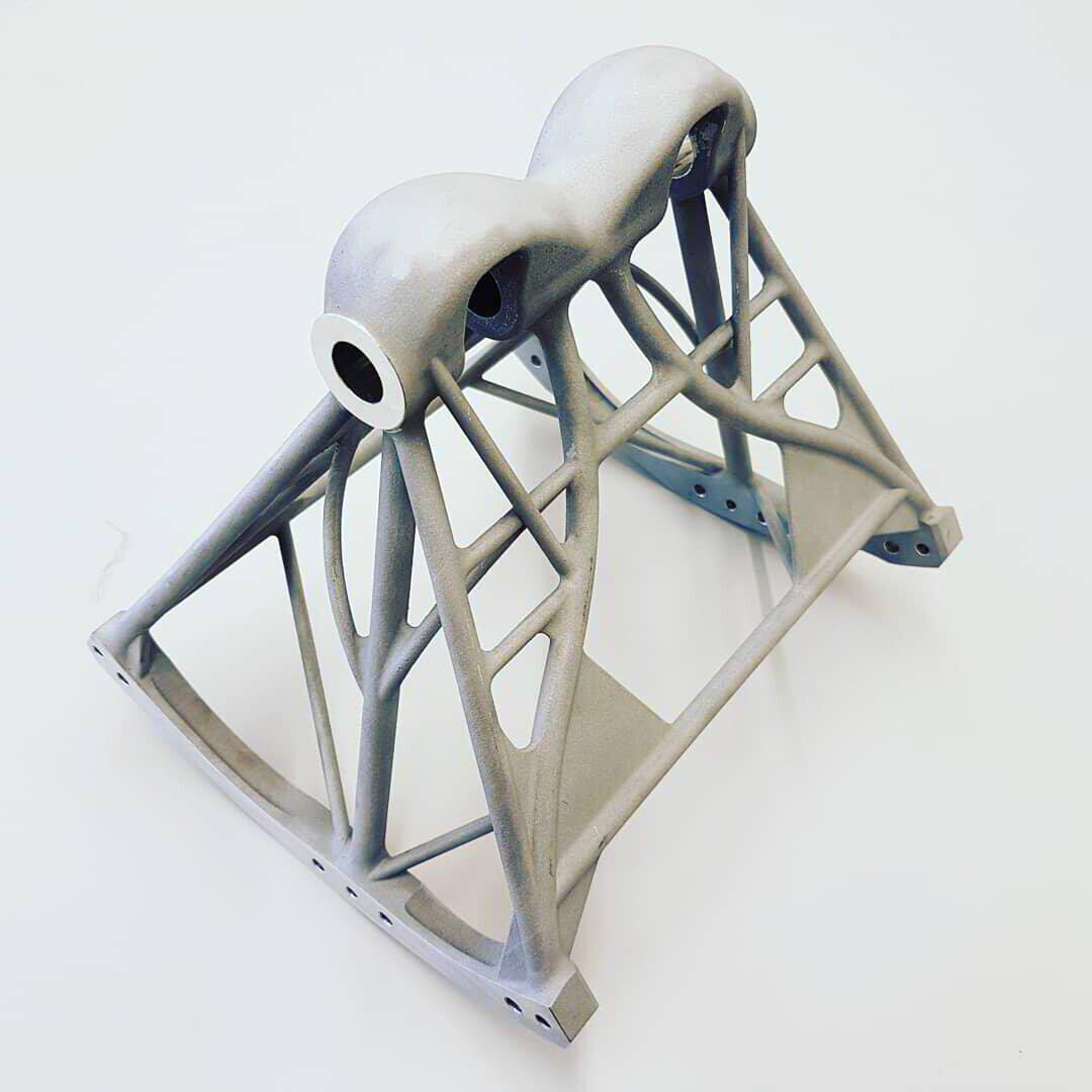 Eine metallische, 3D-gedruckte Strukturkonsole mit einem komplexen, gitterartigen Design und zwei abgerundeten, zylindrischen Halterungen auf weißem Hintergrund.