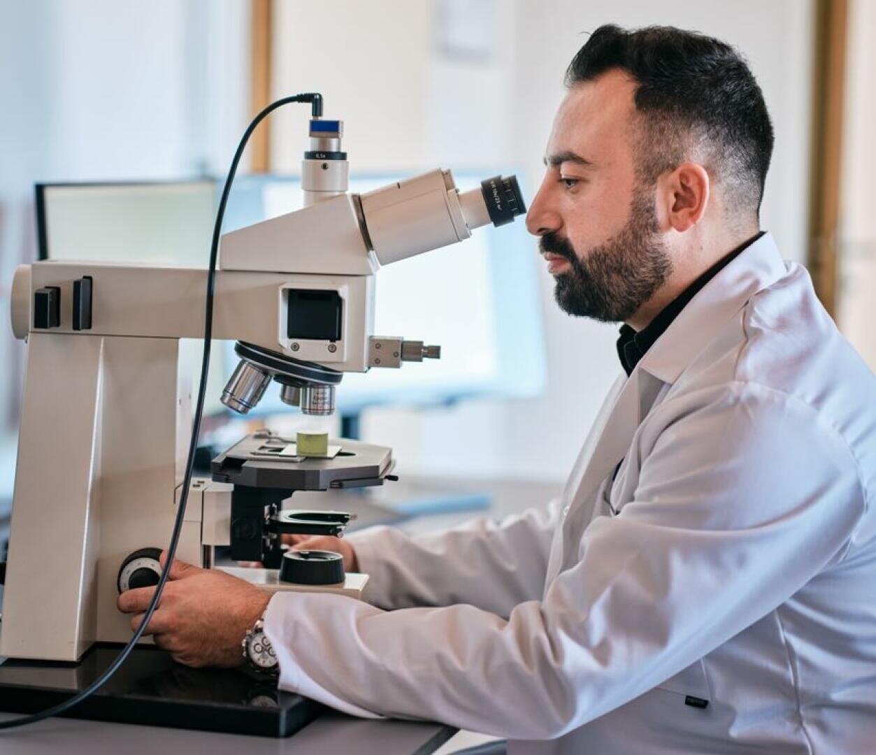 A scientist in a white lab coat examines samples with a microscope in a laboratory environment.