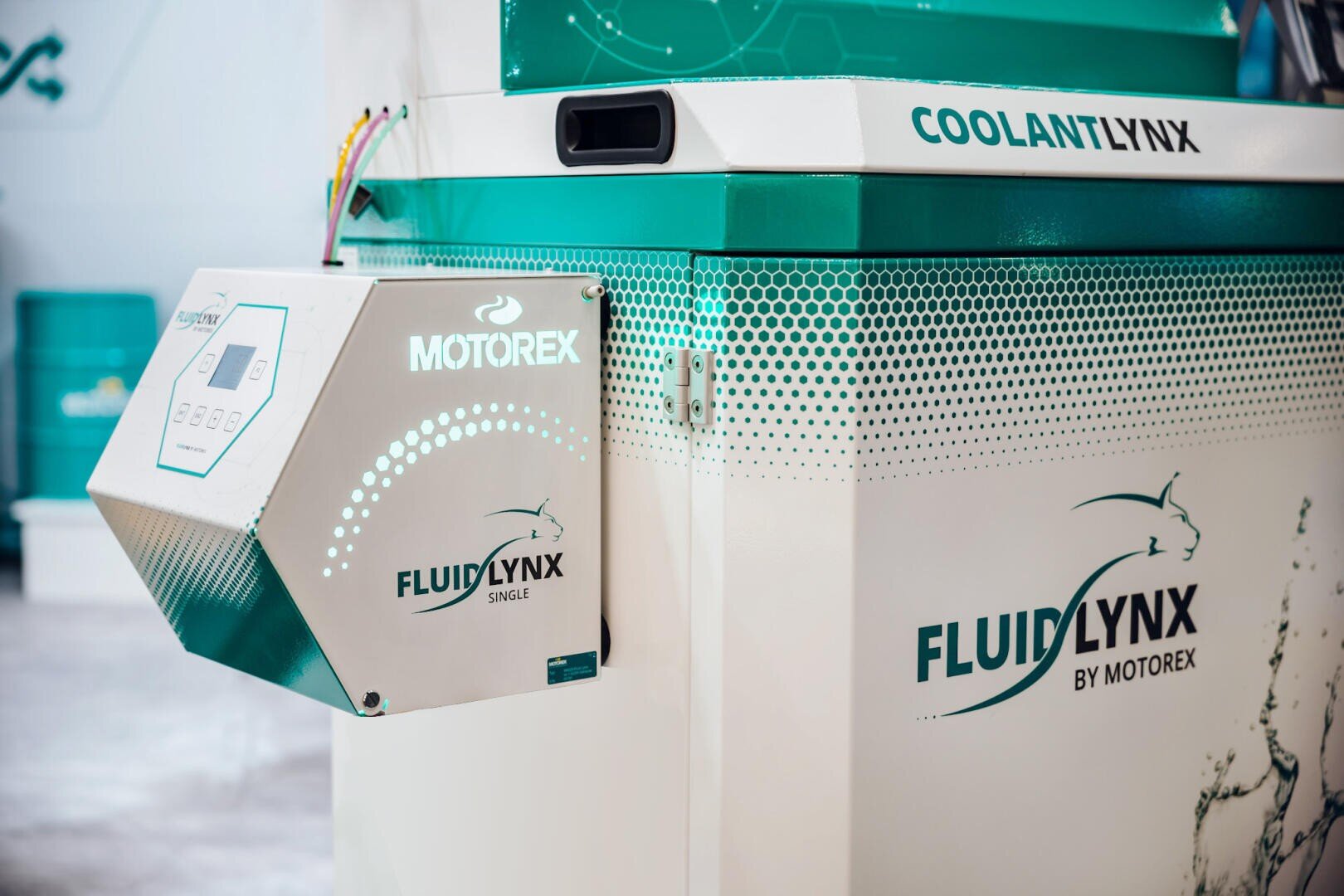 A close-up of a Motorex FluidLynx coolant machine with digital control panel and teal-colored branding with lynx logo. The unit is labeled COOLANT LYNX and FLUIDLYNX BY MOTOREX.
