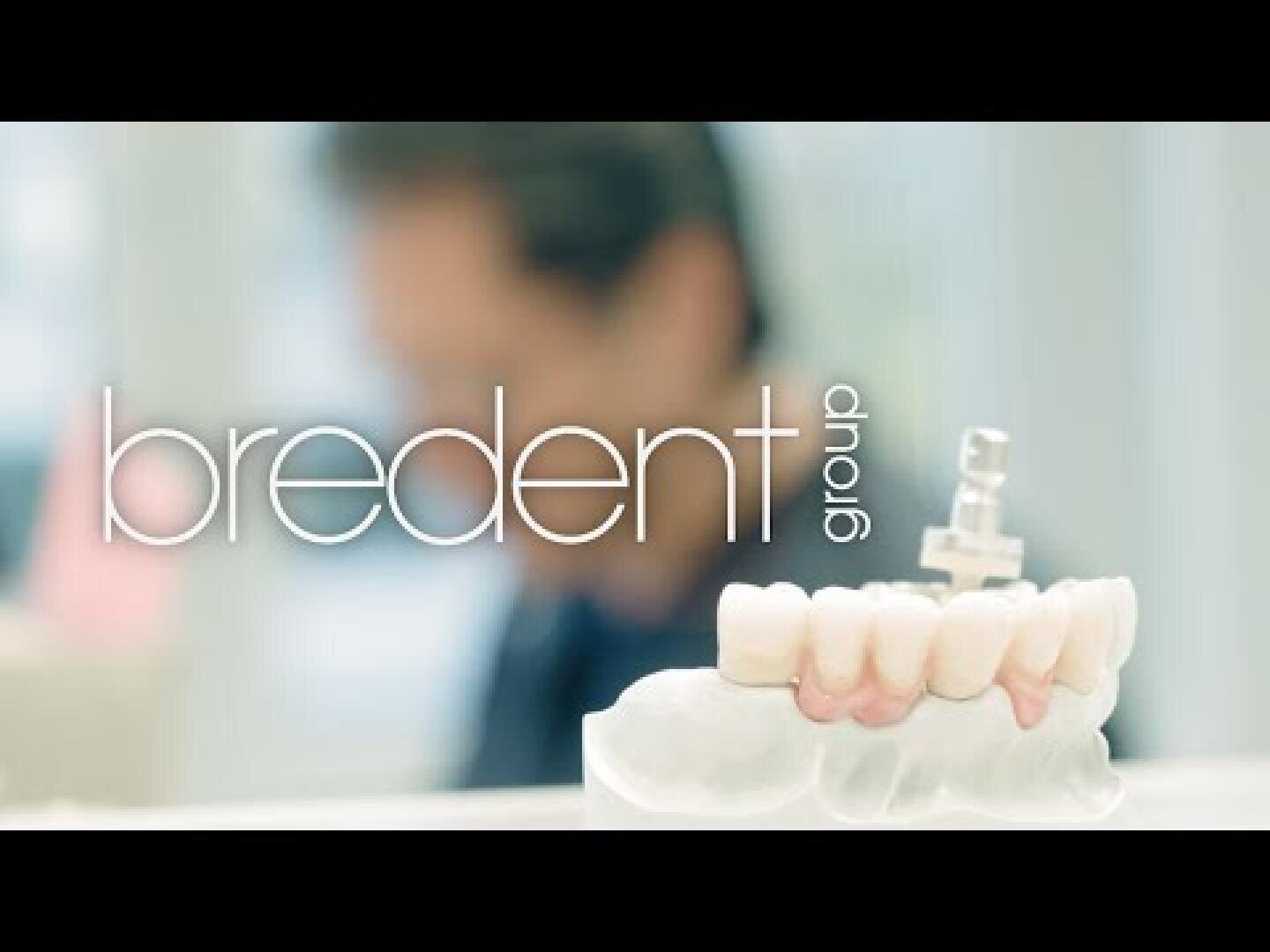 Im Vordergrund ist ein Zahnmodell mit künstlichen Zähnen zu sehen, im Hintergrund die unscharfe Figur einer Person. Der Text bredent group ist über das Bild gelegt.