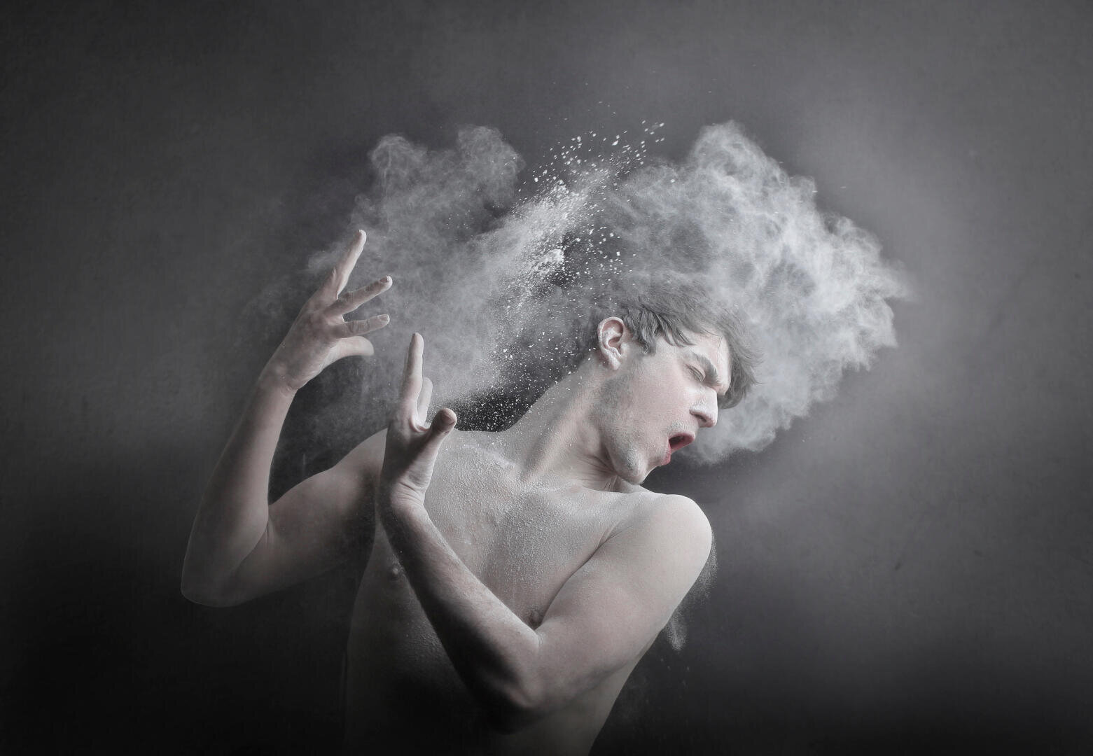 A shirt-sleeved person recoils dramatically as a cloud of white powder surrounds her head and hands, all against a dark gray background.
