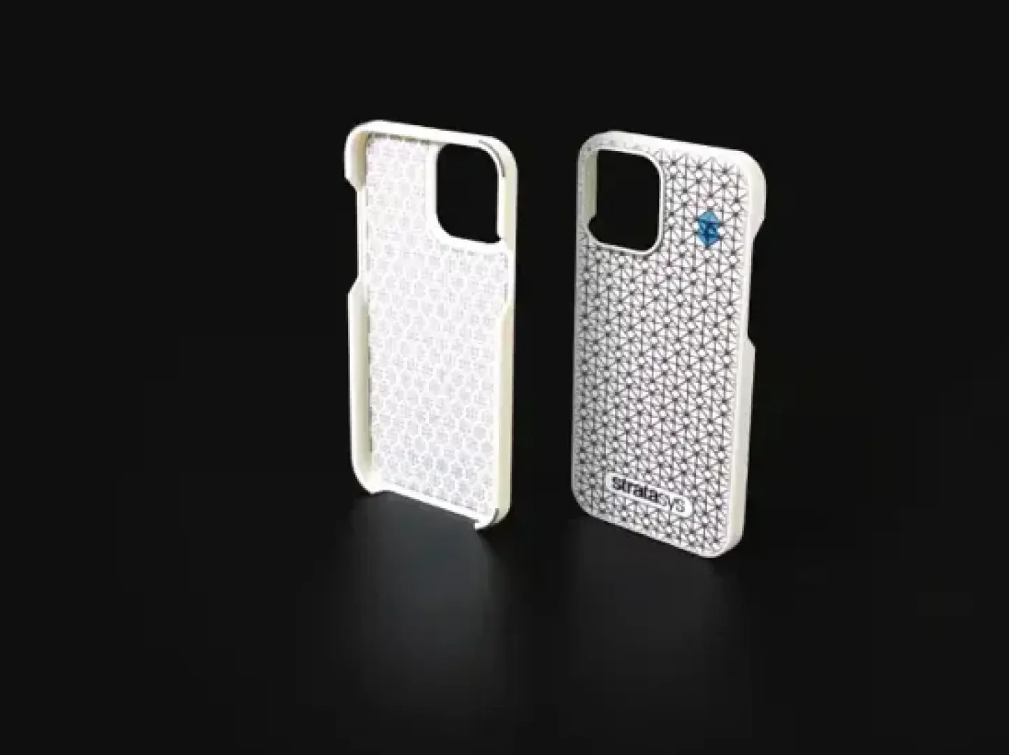 Zwei weiße Smartphone-Hüllen mit einem geometrischen Muster stehen aufrecht auf einer schwarzen Fläche. Ein Gehäuse zeigt ein kleines blaues Detail und das Wort Stratasys in der unteren Ecke.
