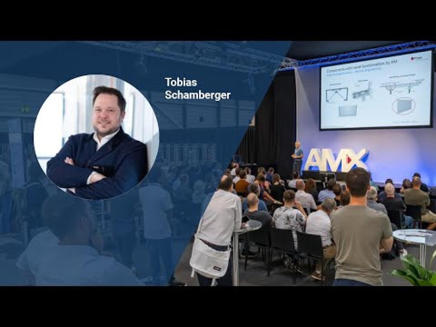 Ein Mann spricht auf der Bühne der AMX-Konferenz zu einem sitzenden Publikum. Auf der linken Seite zeigt ein kreisförmiger Einschub ein Porträt von Tobias Schamberger, dessen Name neben dem Foto erscheint. Hinter dem Redner werden Dias projiziert.