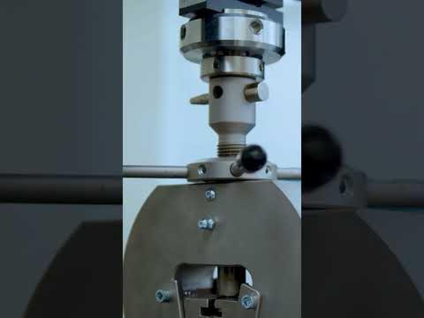 Nahaufnahme einer mechanischen Prüfmaschine mit Metallklemmen und Schrauben, mit denen eine Probe für die Prüfung befestigt wird, wobei verschiedene Einstellknöpfe und Komponenten sichtbar sind.