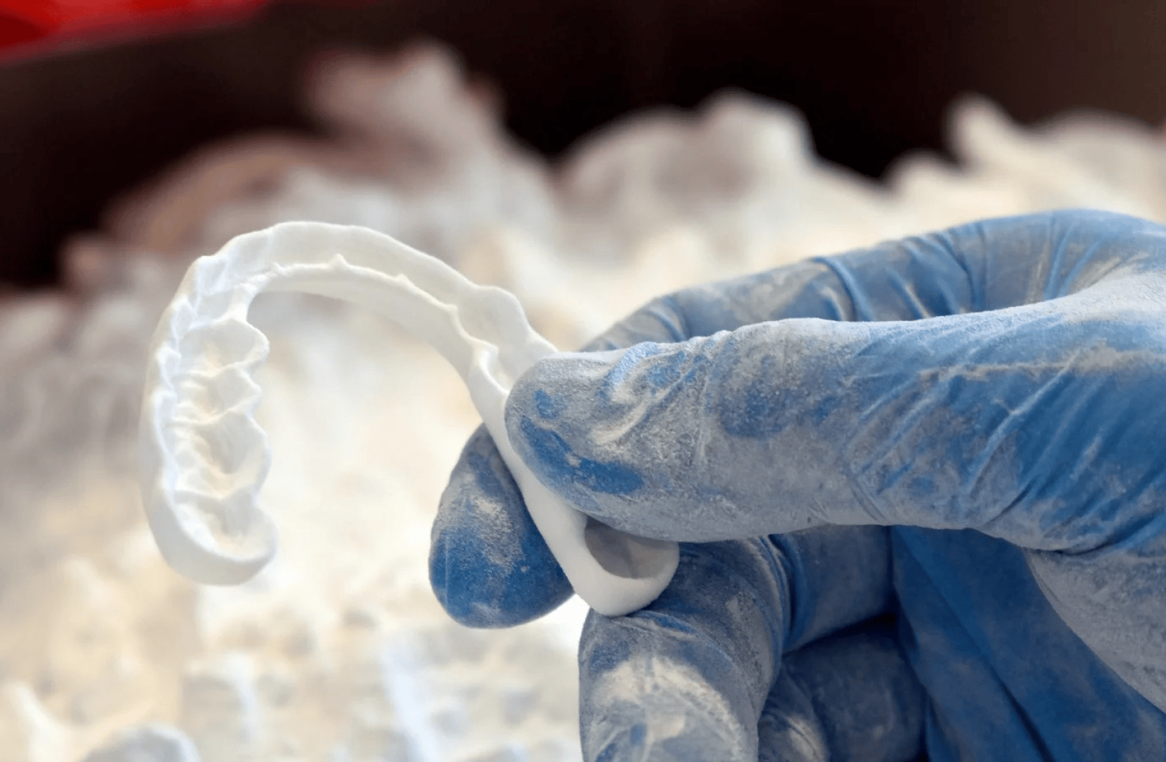 A gloved hand holds a freshly 3D-printed dental splint that is still covered in white powder from the printing process.