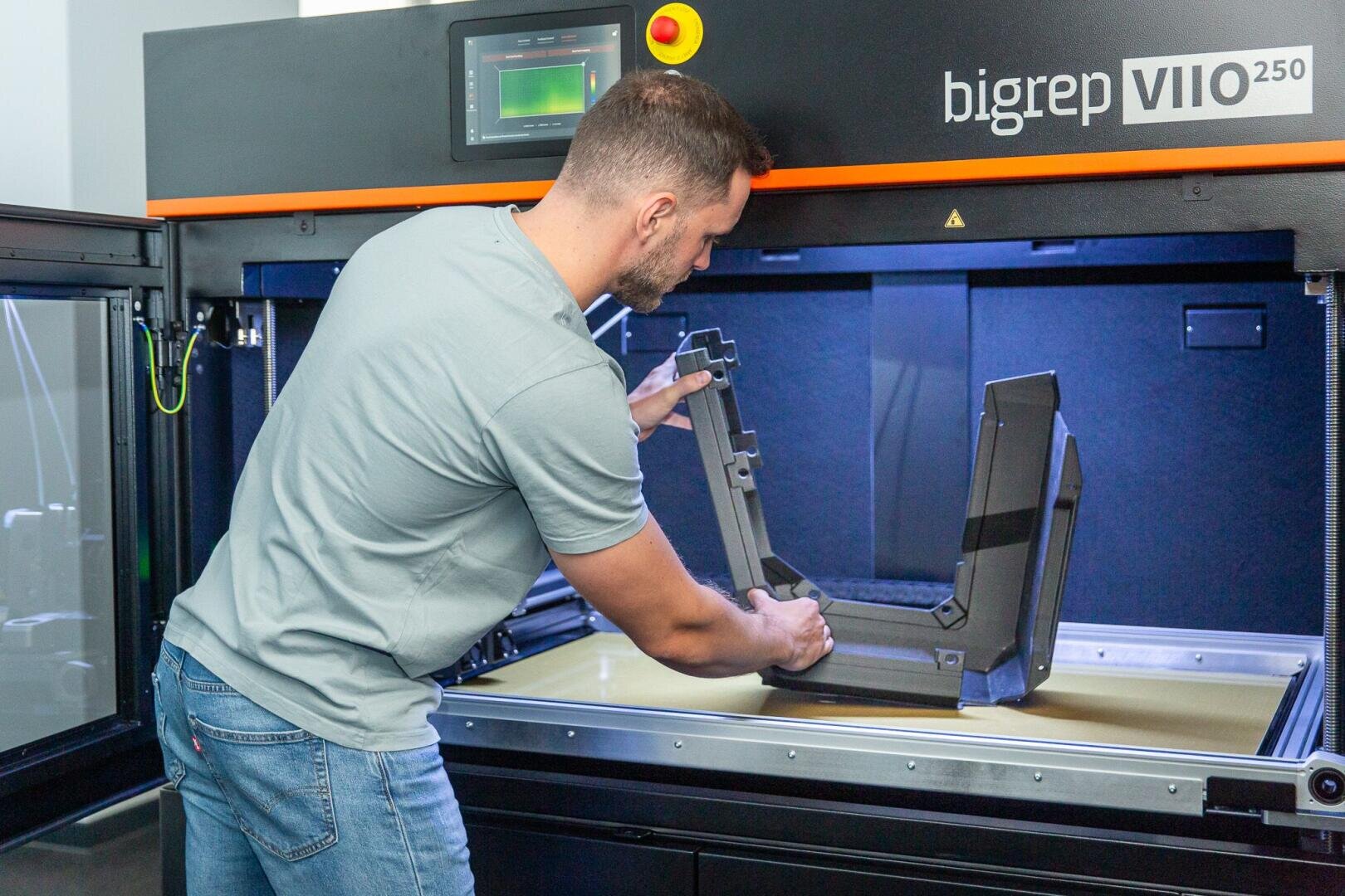 Ein Mann nimmt ein großes 3D-gedrucktes Objekt von der Plattform eines industriellen 3D-Druckers BigRep VIIO 250 ab. Das Innere des Druckers ist sichtbar, und der Mann geht vorsichtig mit dem gedruckten Objekt um.