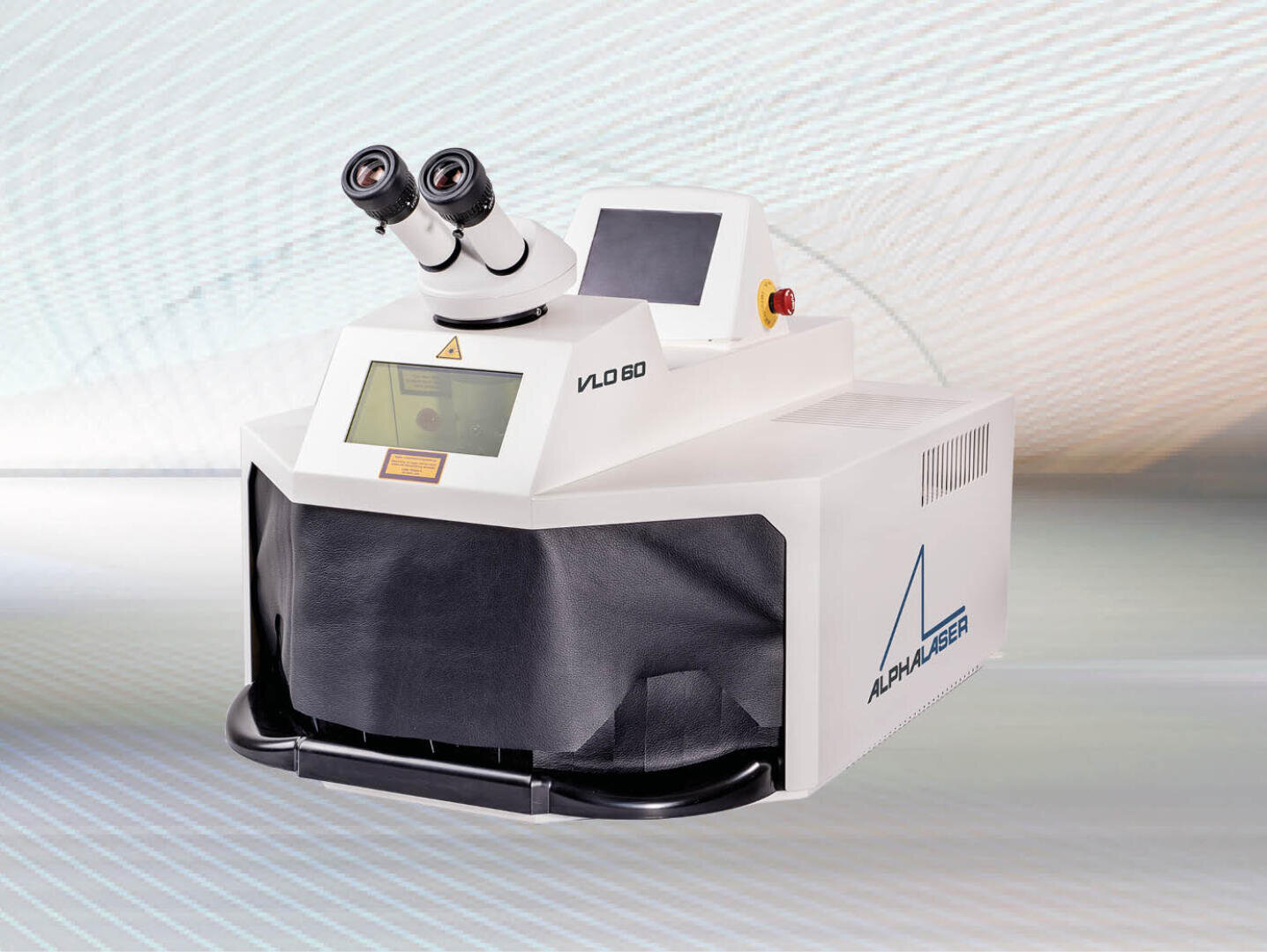 Ein weißes Tisch-Laserschweißgerät mit zwei Okularen, einer digitalen Anzeige und einem Bedienfeld mit den Aufschriften VLO 60 und ALPHALASER auf einem hellen gemusterten Hintergrund.
