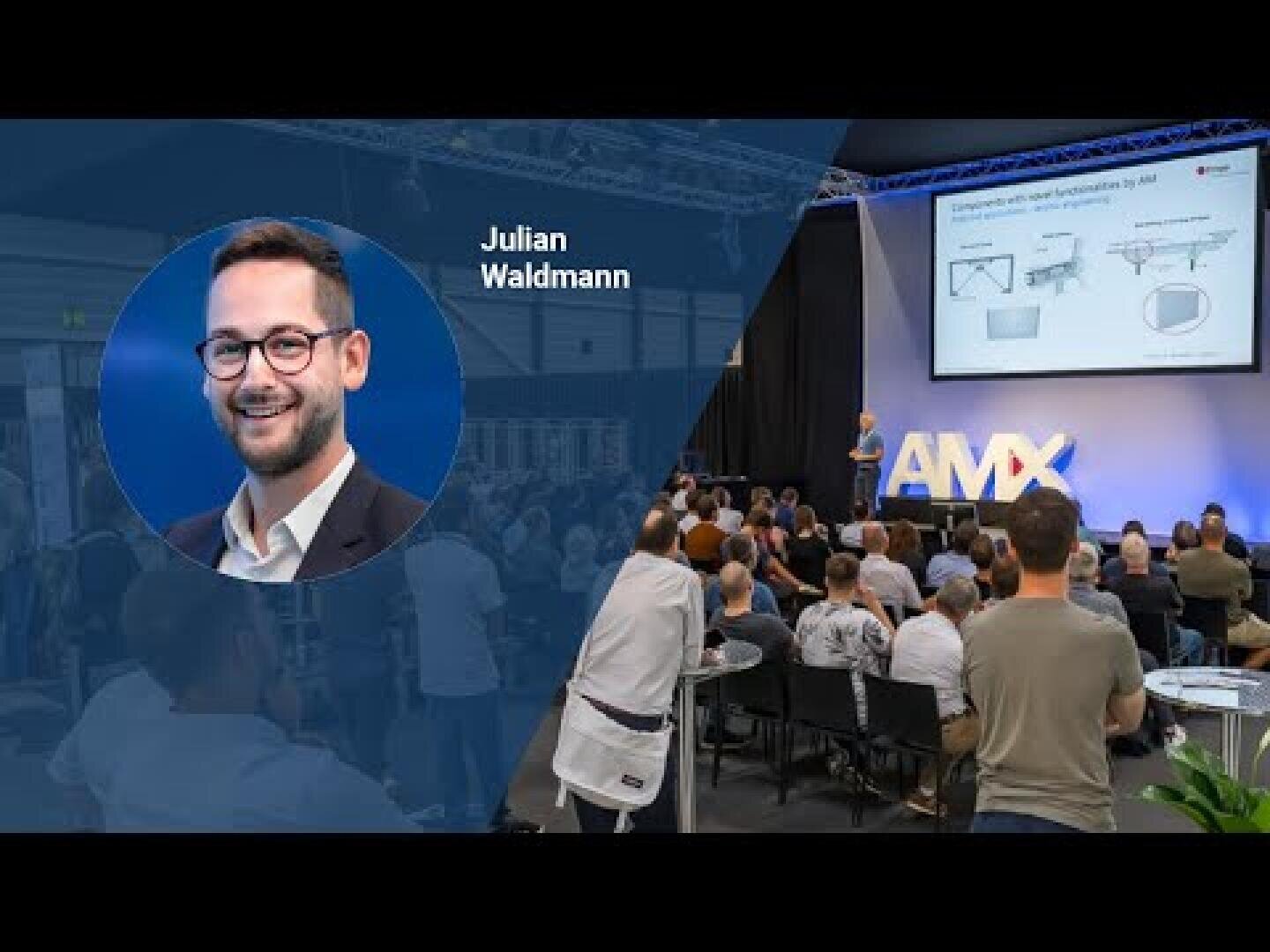 A man named Julian Waldmann is highlighted on the left side, while on the right, an audience watches a presentation in a large event space with a screen displaying technology-related visuals and the letters AMX.
