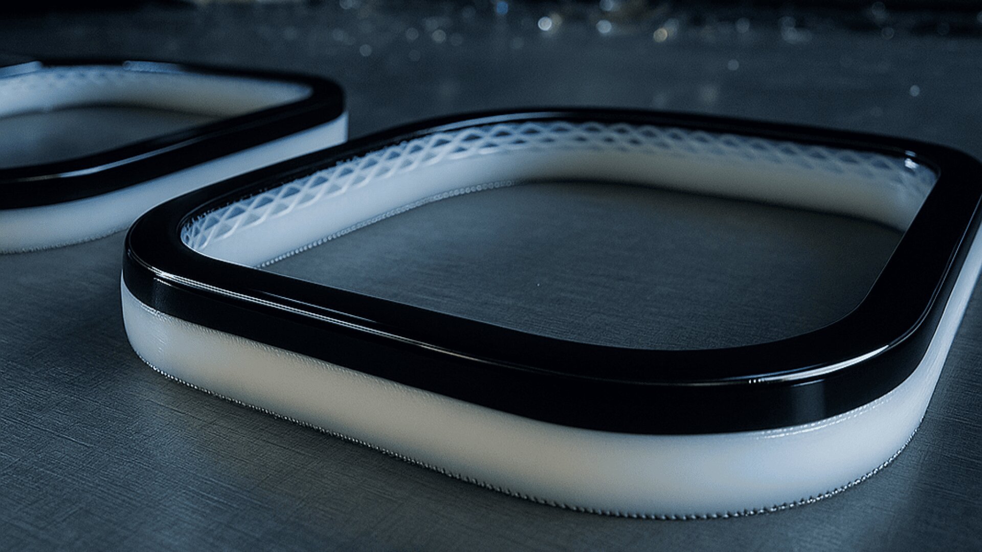 Close-up of two black and white rectangular frames with rounded edges, lying flat on a metallic surface. The frames have a smooth finish and a patterned inner edge visible in the foreground.