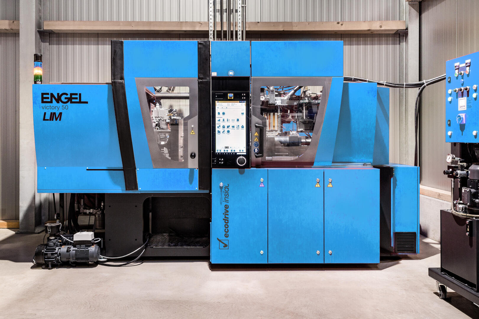 Eine große blaue ENGEL victory 50 LM Spritzgießmaschine mit zentralem Touchscreen-Bedienfeld steht in einer gut beleuchteten Industriehalle.